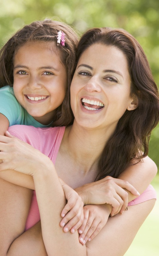 Woman and young girl embracing outdoors smiling